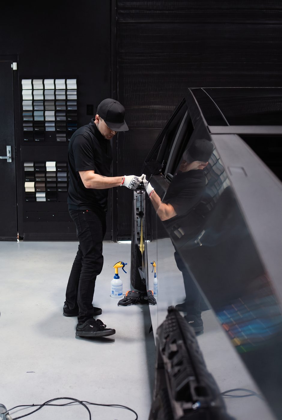Installer preparing a glossy black vehicle panel for vinyl wrap inside the High Society Customs shop
