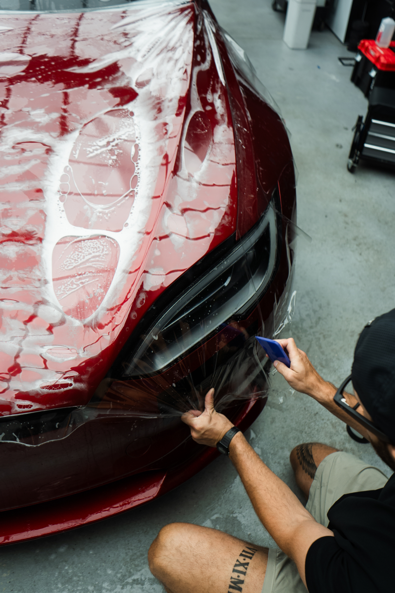 Installer applying paint protection film to the front bumper of a red sports car