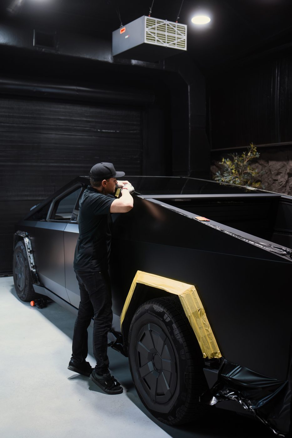 Matte black vinyl wrap being applied to the rear quarter panel of a Cybertruck