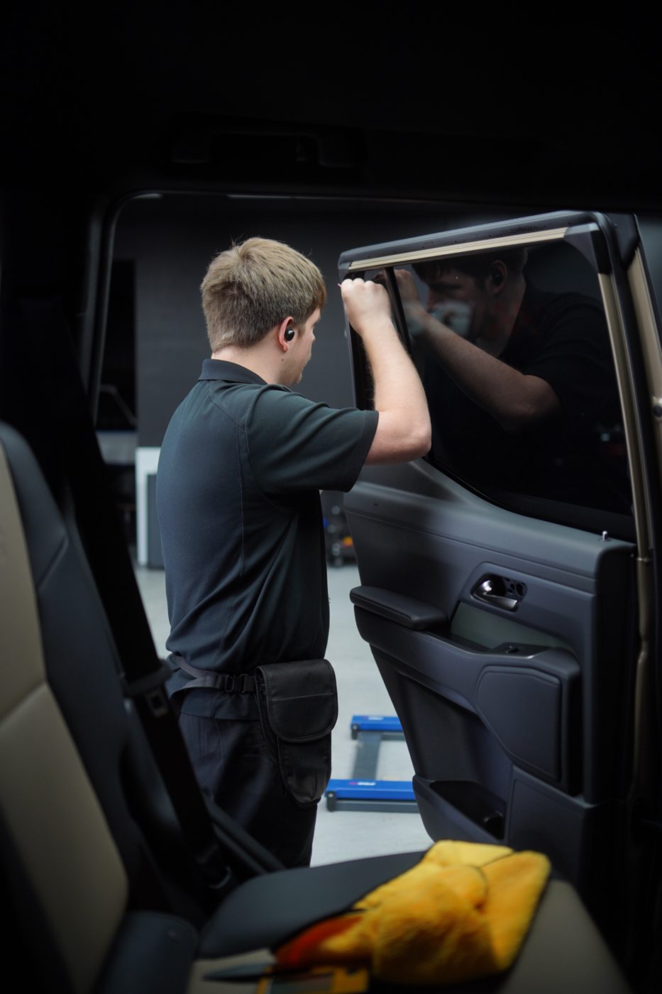 Installer applying window tint film to a car door glass inside the shop
